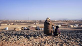 Ein Vater und sein siebenjähriger Sohn sitzen auf einem Hügel und schauen hinunter auf das Geflüchtetencamp Alswidan in Marib (Jemen). Weit und breit sind nur trostlose Steinwüste und einige Zelte zu sehen.