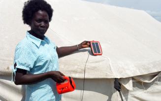 Mary demonstriert vor ihrem Zelt in einem Camp im Südsudan, wie sie ihre Solarlampe in der Sonne auflädt. Frau mit Solarlampe in einem Camp für Geflüchtete im Südsudan