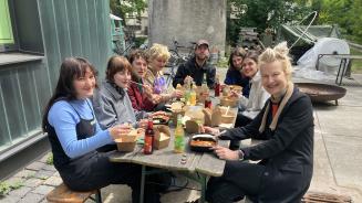 Mehrere junge Menschen sitzen sich auf Bänken an einem Aufklapptisch gegenüber und essen gemeinsam.