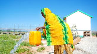 Eine Frau füllt einen gelben Wasserkanister an einer Wasserleitung.