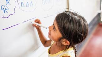 Eine junge Schülerin schreibt etwas auf eine Schultafel
