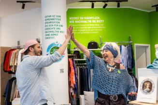 Zwei Personen stehen in einem Oxfam-Shop und geben einander ein High-Five.