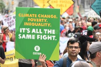 Der Vorsitzende von Oxfam International, Amitabh Behar, hält ein Protestschild gegen fossile Brennstoffe hoch.