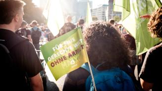 Protestierende mit Fahnen. Im Vordergrund eine Fahne mit dem Oxfam-Slogan „Für eine gerechte Welt. Ohne Armut“.