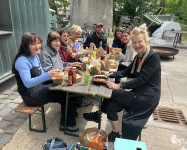 Mehrere junge Menschen sitzen sich auf Bänken an einem Aufklapptisch gegenüber und essen gemeinsam.