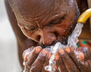 Ein Mann fängt Wasser aus einem Wasserhahn mit den Händen auf und trinkt.