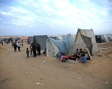 Gaza braucht Frieden Eine Szene aus einem Camp in Rafah, Gaza. Kinder bereiten essen vor einem Zelt zu. Menschen teilen Wasser aus.