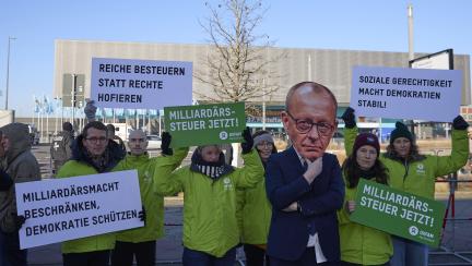 Mehrere Menschen mit Plakaten und ein Mensch mit Friedrich-Merz-Maske