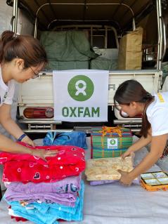 Zwei weiblich gelesene Personen in Oxfam-Shirts packen Kleidungsstücke und Handtücher zusammen.