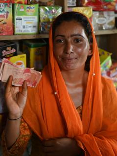 Eine Frau steht vor einem Regal mit Lebensmitteln und zeigt einige Geldscheine.