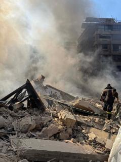 Nach Israels nächtlichem Bombenangriff auf die südlichen Vororte von Beirut durchsuchen Rettungskräfte die Trümmer. Die Trümmer eines Hauses zwischen anderen Gebäuden. Es steigt Rauch auf. Zwei Menschen bewegen sich über die Trümmer.