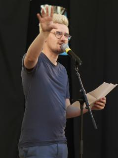 Zwei Männer sprechen in Mikrofone. Sie halten jeweils ein Blatt Papier in der Hand.