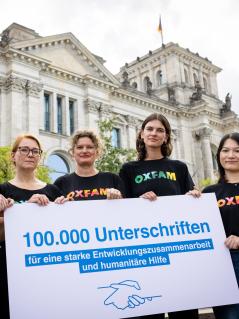 Fünf Personen stehen auf einer Treppe vor dem Bundestag und halten ein Schild mit der Aufschrift: 100.000 Unterschriften für eine starke Entwicklungszusammenarbeit und humanitäre Hilfe.