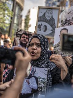 Rima Azzaher macht ein Statement inmitten einer Menschenmenge. Sie hält ein Foto ihres verstorbenen Bruders in den Händen.