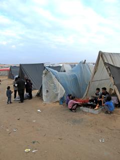Eine Szene aus einem Camp in Rafah, Gaza. Kinder bereiten essen vor einem Zelt zu. Menschen teilen Wasser aus.
