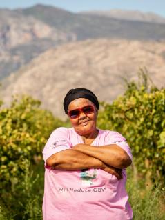 Fransiena van Rooi steht auf einer Weinplantage in Western Cape, Südafrika. Die trägt eine Sonnenbrille, hat die Arme verschränkt und blickt selbstbewusst in die Kamera.
