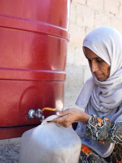 Eine syrische Frau aus Deir Ez-Zor füllt ihren Kanister mit Wasser aus einem Gemeinschaftstank.