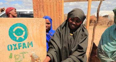 Mehrere Frauen stehen an einem von Oxfam errichteten Wassertank und füllen ihre Flaschen auf.