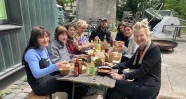 Mehrere junge Menschen sitzen sich auf Bänken an einem Aufklapptisch gegenüber und essen gemeinsam.