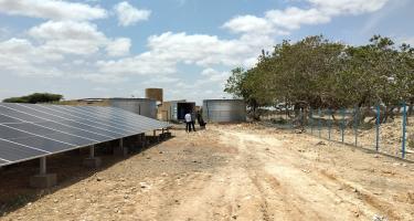 Solarpaneele und ein großer Wassertank. Sehr weit hinten im Bild unterhalten sich mehrere Menschen.