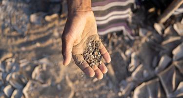 Bakeel Saif Jahes zeigt verdorrte Erde von seiner Farm in Al-Wahat in der Provinz Lahj im Jemen. Seine Arbeit wurde schon lange durch Dürre erschwert. Doch dann haben schwere Überschwemmungen seine Felder, seine Vorräte und seine gesamte Farm zerstört. Wetterextreme wie diese werden durch den Klimawandel wahrscheinlicher. Bakeel Saif Jahes hält eine Handvoll trockene, staubige Erde in die Kamera.