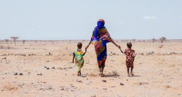 Eine Frau läuft Hand in Hand mit zwei Kleinkindern durch eine Wüstenlandschaft.