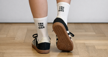 Tennissocken mit der Aufschrift „Tax the Rich“ (Reiche besteuern) an zwei Füßen.
