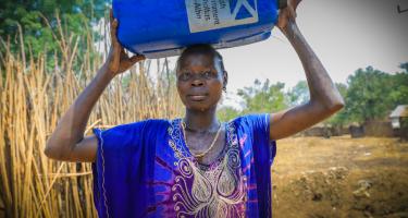 Eine Frau trägt einen Wasserkanister auf dem Kopf.