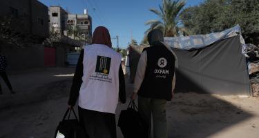 Zwei Frauen mit großen Taschen in Rückenansicht. Eine trägt eine Weste der Organisation Juzoor, die andere eine Weste von Oxfam.