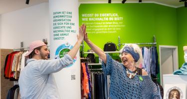 Zwei Personen stehen in einem Oxfam-Shop und geben einander ein High-Five.