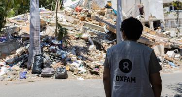 Eine Person in Oxfam-Weste. Im Hintergrund Trümmer.