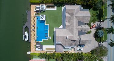 Luftaufnahme einer Villa mit Fuhrpark, Pool, Boot und Anlegestelle