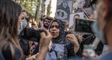 Rima Azzaher macht ein Statement inmitten einer Menschenmenge. Sie hält ein Foto ihres verstorbenen Bruders in den Händen.