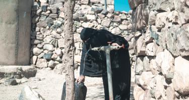 Haneen* (in schwarzem Gewand und mit Niqab bekleidet) dreht einen Wasserhahn vor ihrem Haus auf, um einen Wasserkanister zu befüllen.