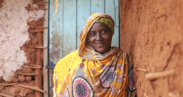 Eine Frau lächelt in die Kamera. Sie lehnt an einer Wand, ihr Blick ist selbstsicher und stolz.