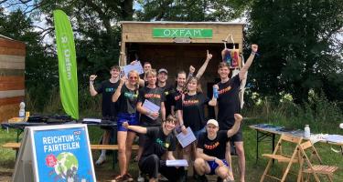 Eine Gruppe von Oxfam-Aktiven posiert mit Unterschriftenlisten vor dem Oxfam-Stand auf einem Festival