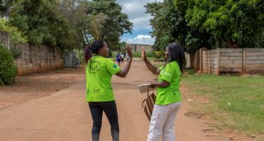 Abigail und Shylet geben sich ein High-Five auf dem Weg nachhause. Sie tragen grüne T-Shirts mit der Aufschrift "Champions-Care Work"