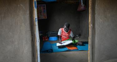 Deng, ein Grundschüler in Palabek, Uganda, lernt allein. Ein Junge sitzt auf einer Matte und schreibt in ein Heft