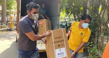 Oxfam-Mitarbeiter laden einen Sauerstoffkonzentrator aus einem Lastwagen aus. Zwei Mitarbeiter von Oxfam Indien tragen einen Karton mit einem Sauerstoffkonzentrator.