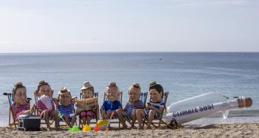 Aktivist*innen posieren als G7-Regierungschef*innen am Strand. Sie tragen gestreifte Badesachen und Sonnenhüte.