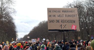 "Die einzige Minderheit, die die Welt ruiniert, sind die reichsten 1 %" viele Menschen mit Demoschildern bewegen sich auf den Großen Stern in Berlin zu. Auf einem Schild steht "Die einzige Minderheit, die die Welt ruiniert, sind die reichsten 1 %"