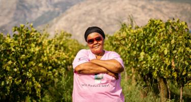 Fransiena van Rooi ist Aktivistin in unserer langjährigen Partnerorganisation Women on Farms Project. Fransiena van Rooi steht auf einer Weinplantage in Western Cape, Südafrika. Die trägt eine Sonnenbrille, hat die Arme verschränkt und blickt selbstbewusst in die Kamera.