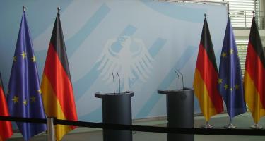 Flaggen der Europäischen Union und der Bundesrepublik Deutschland hängen neben zwei mikrofonierten Redepulten