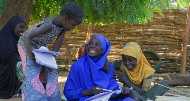 Drei Kinder sitzen auf dem Boden und schreiben in ihre Schulhefte