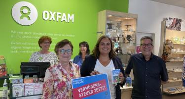 In einem Oxfam Shop übergeben Menschen Postkarten mit der Aufschrift „Reichtum fairteilen – Vermögenssteuer jetzt!“ an die Isabel Cademartori
