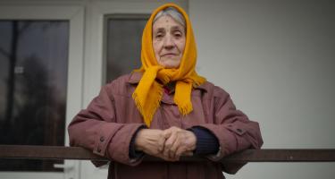 Tamara Dmytrivna lebt in einer Unterkunft für Vertriebene in Mykolaiv. Unsere Partnerorganisation The Tenth of April half ihr bei der Evakuierung und sicherte ihr einen Platz in der Unterkunft, wo sie mit ihrer Tochter wohnt. Die Organisation unterstützt Vertriebene außerdem bei rechtlichen Dokumenten und Registrierungen und bietet psychosoziale Hilfe. Tamara Dmytrivna steht auf einem Balkon. Sie schaut ernst in die Kamera.