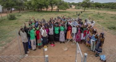 Eine Gruppe von Menschen steht bei einer Wetterstation in einer ländlichen Region in Simbabwe. Sie strecken freudig ihre Arme in die Luft.