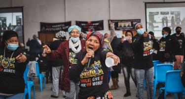 Eine Gruppe von Farmarbeiterinnen singen auf einer Protestaktion mit schwarzen Tshirts mit der Aufschrift "Thulas, give us our money".