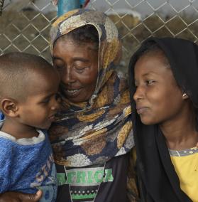 Eine Frau hat ihre Kinder im Arm. Sie lächeln sich an.