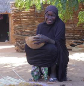Ein Frau sitzt vor ihrem Haus und hält eine Schüssel in der Hand